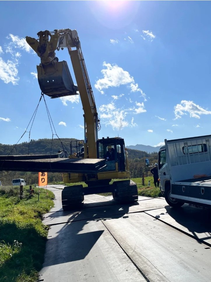 公共土木工事の仮設道路。バックホウのクレーンでCLTmatを吊り上げて設置